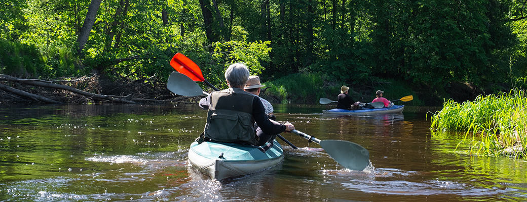 Image of senior couple paddling in a kayak down a serene river
